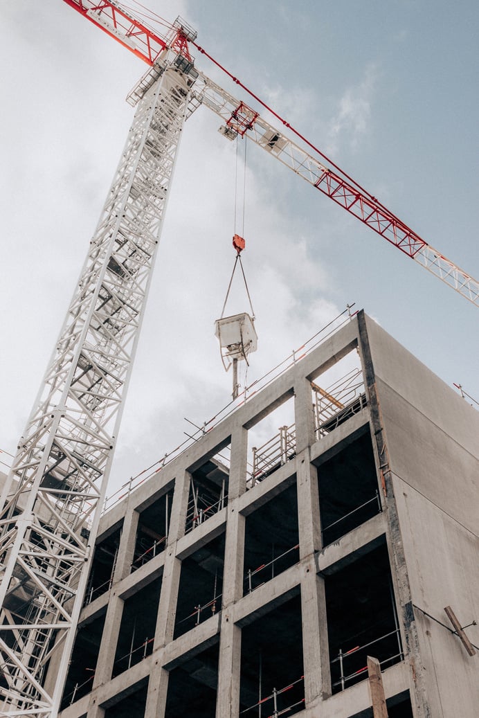 Half built multistage building and crane tower at construction area against cloudy sky